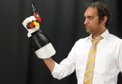 A man wears a prosthetic robotic glove, and with that he holds an electric drill.